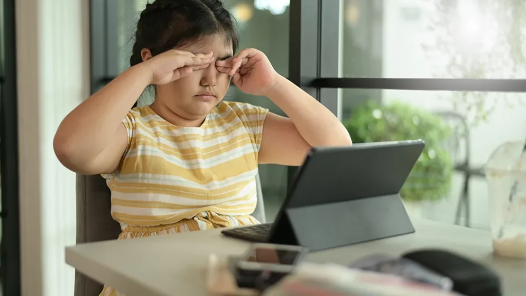 child rubbing tired eyes at a tablet